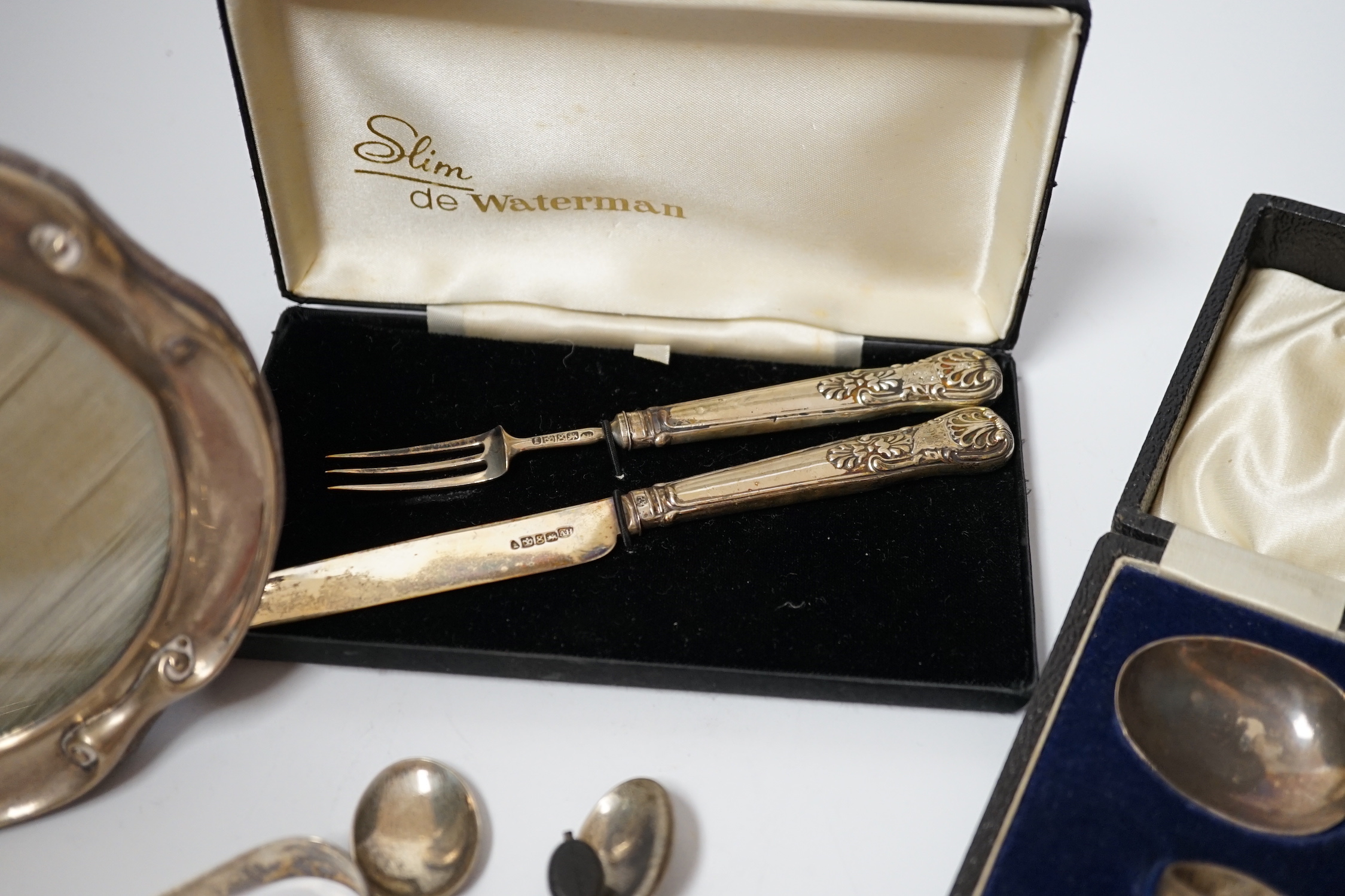 A cased silver christening spoon & pusher, a Georgian silver christening knife and fork, six silver bean end coffee spoons, a child's silver rattle, silver sugar tongs and a silver mounted photograph frame, Birmingham, 1